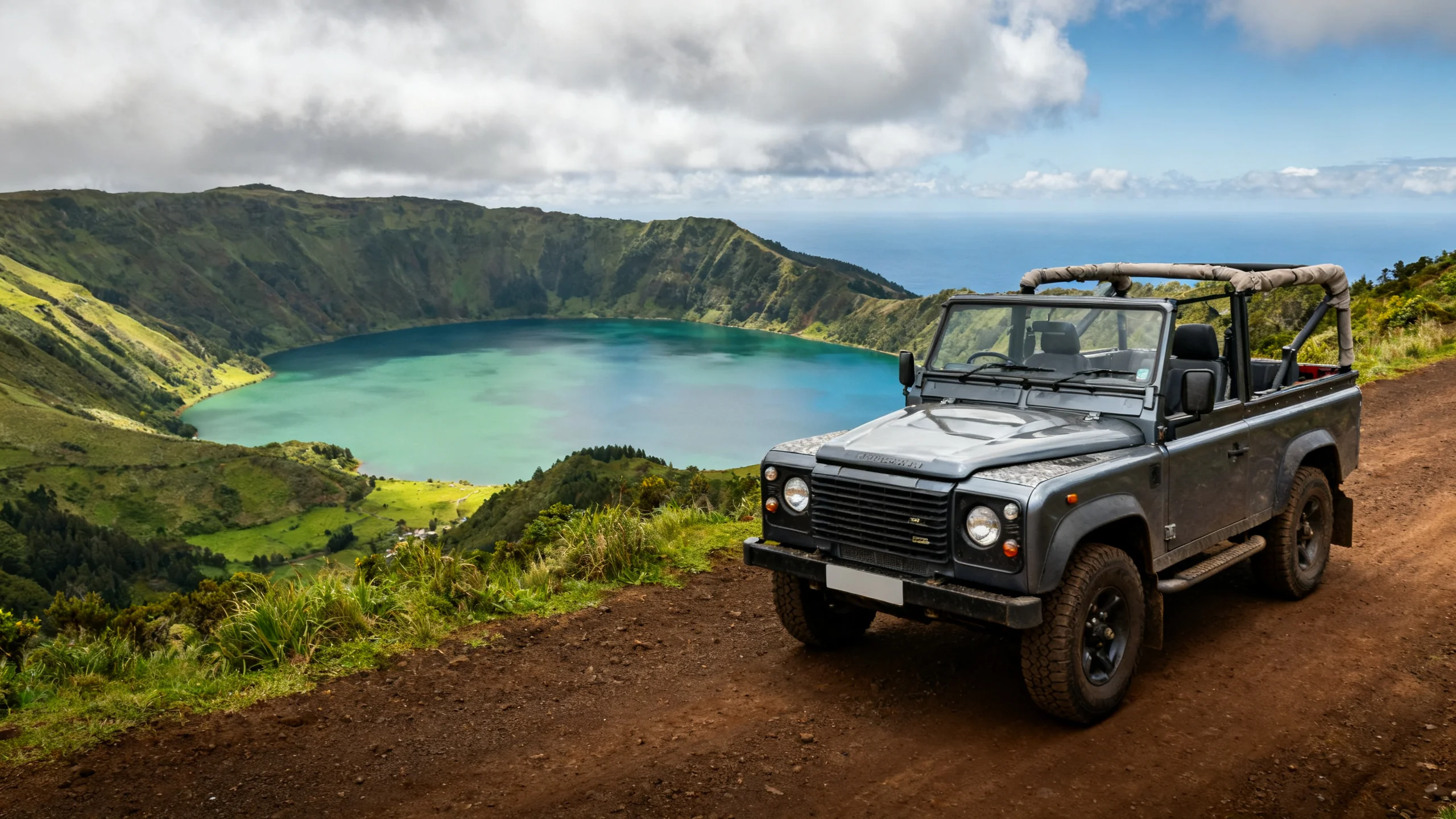 Jeep 4x4 décapotable sur un chemin de terre surplombant la caldeira de Sete Cidades avec les lacs jumeaux vert et bleu visibles en contrebas